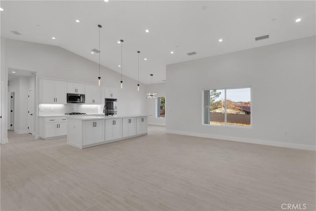 kitchen with light wood-type flooring, pendant lighting, a center island with sink, high vaulted ceiling, and white cabinetry