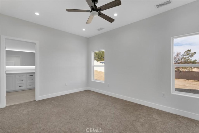 unfurnished bedroom with light carpet, connected bathroom, multiple windows, and ceiling fan