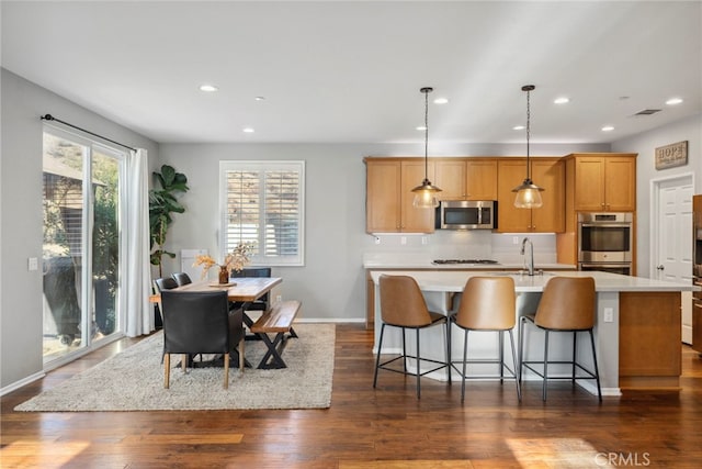 kitchen featuring stainless steel appliances, decorative light fixtures, an island with sink, decorative backsplash, and dark hardwood / wood-style floors