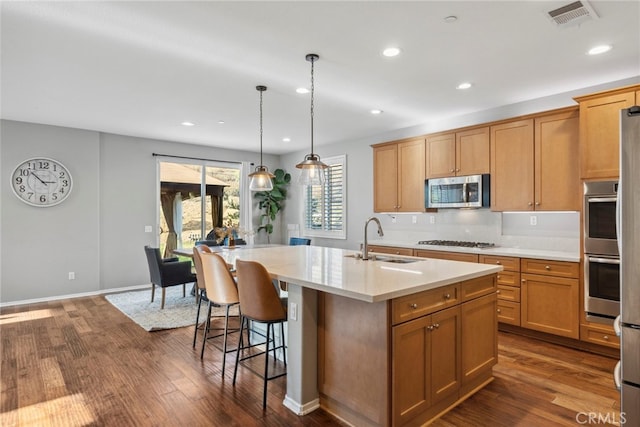 kitchen with pendant lighting, dark hardwood / wood-style floors, stainless steel appliances, a kitchen island with sink, and sink