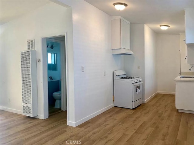 kitchen with white cabinets, white gas range, sink, and light hardwood / wood-style flooring