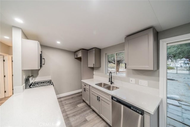 kitchen featuring stove, light wood-type flooring, sink, dishwasher, and gray cabinets