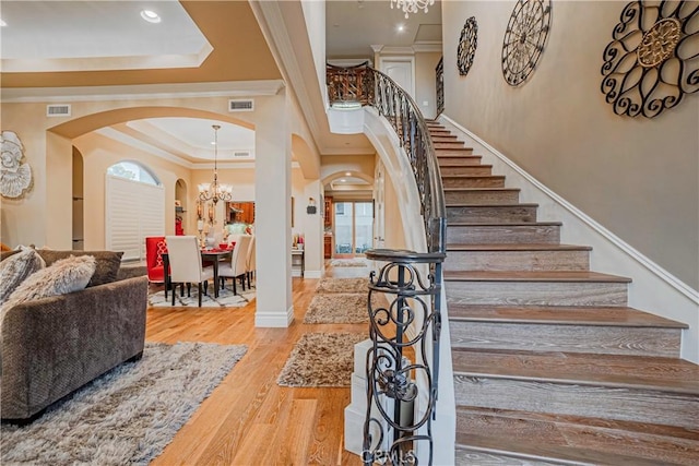 stairs with hardwood / wood-style floors, a raised ceiling, crown molding, and an inviting chandelier