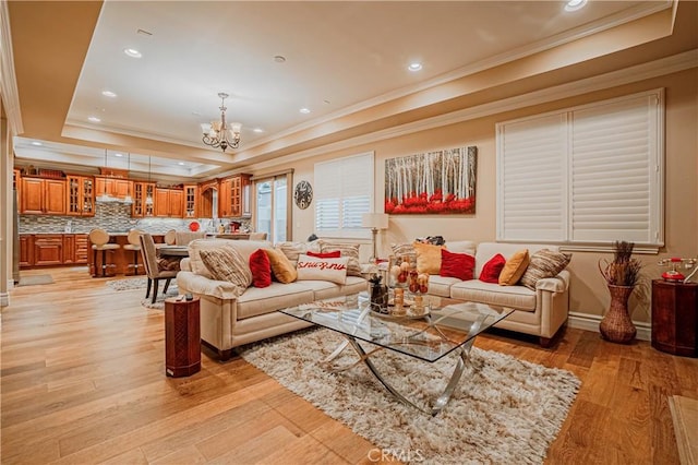 living room with a notable chandelier, light hardwood / wood-style floors, crown molding, and a tray ceiling