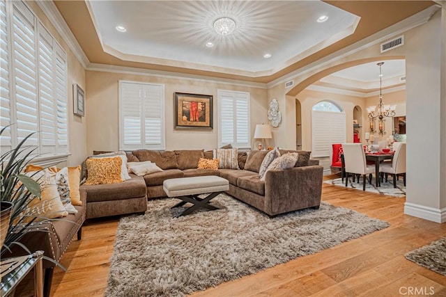 living room featuring a raised ceiling, an inviting chandelier, light hardwood / wood-style flooring, and crown molding