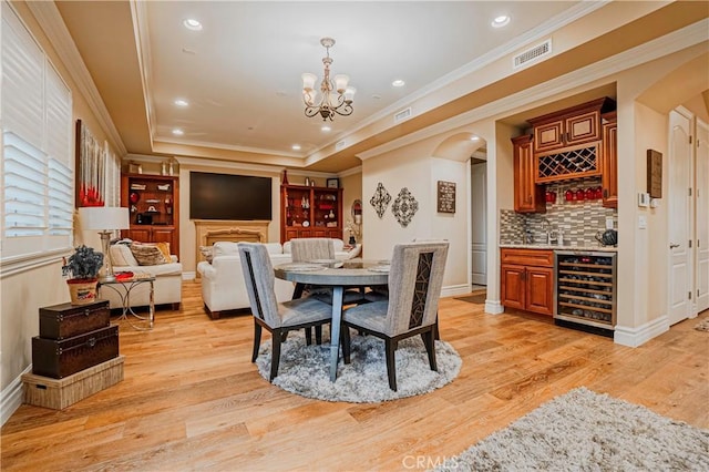 dining space featuring wine cooler, crown molding, light hardwood / wood-style floors, and indoor bar