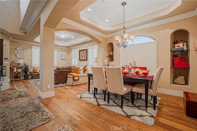 dining room with a chandelier, light hardwood / wood-style floors, a raised ceiling, and ornamental molding