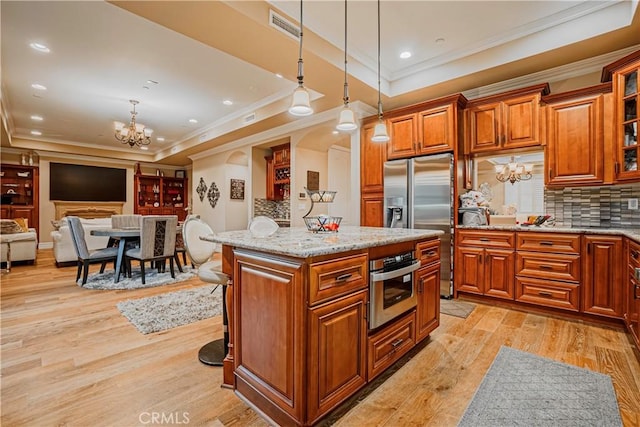 kitchen featuring a kitchen island, a raised ceiling, hanging light fixtures, and appliances with stainless steel finishes