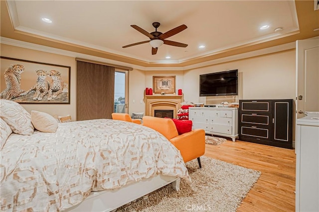 bedroom featuring ceiling fan, light hardwood / wood-style floors, crown molding, and a tray ceiling