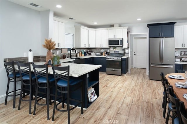 kitchen featuring sink, light wood-type flooring, appliances with stainless steel finishes, tasteful backsplash, and white cabinetry