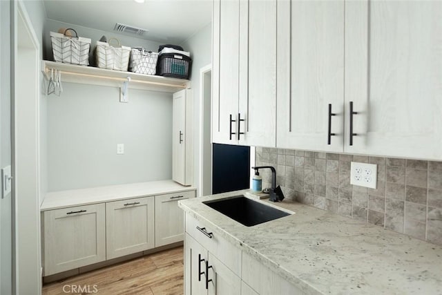 kitchen featuring tasteful backsplash, light stone countertops, sink, and light hardwood / wood-style flooring