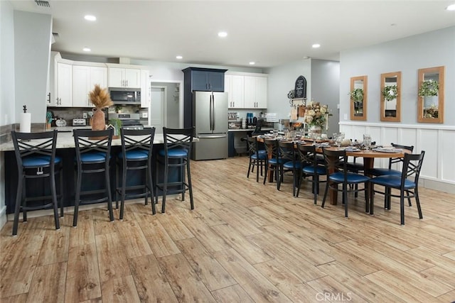 kitchen featuring white cabinetry, a kitchen bar, light wood-type flooring, and stainless steel appliances