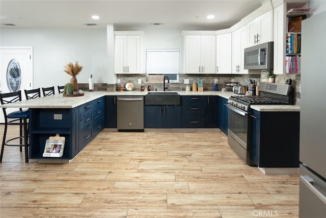 kitchen featuring a kitchen bar, stainless steel appliances, blue cabinets, sink, and white cabinets