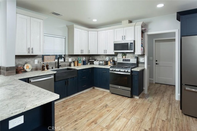 kitchen with appliances with stainless steel finishes, light wood-type flooring, tasteful backsplash, sink, and white cabinetry