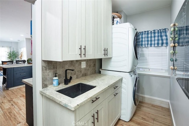 kitchen featuring light stone counters, sink, stacked washing maching and dryer, and light hardwood / wood-style flooring