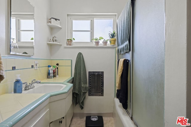 bathroom with tasteful backsplash, tile patterned flooring, heating unit, shower / bath combination with glass door, and vanity