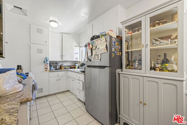 kitchen with light stone countertops, stainless steel fridge, white cabinetry, and light tile patterned flooring