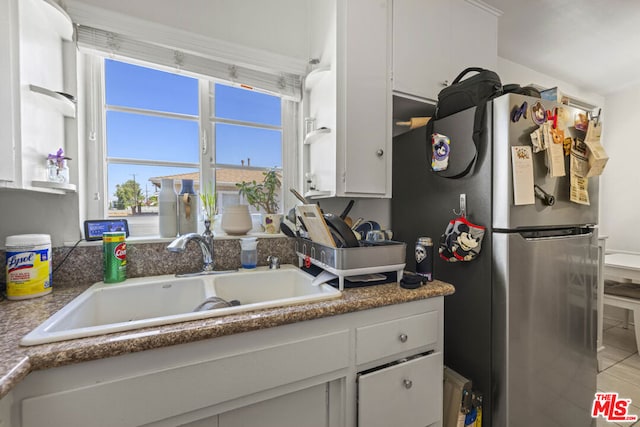 kitchen with white cabinetry, sink, and stainless steel refrigerator