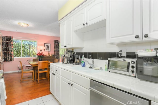 kitchen with white cabinetry, sink, stainless steel dishwasher, tile countertops, and light hardwood / wood-style floors