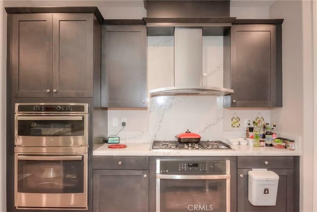 kitchen featuring tasteful backsplash, dark brown cabinetry, wall chimney exhaust hood, and stainless steel appliances