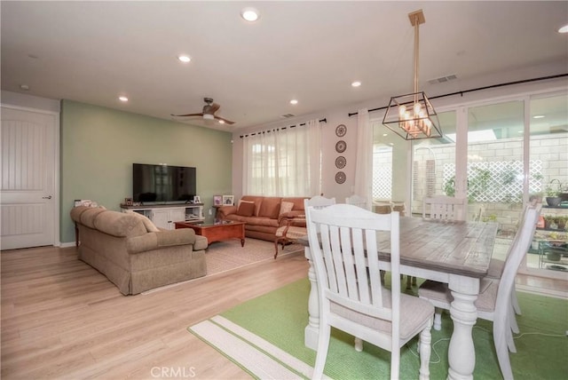 dining room with ceiling fan with notable chandelier, light hardwood / wood-style floors, and plenty of natural light