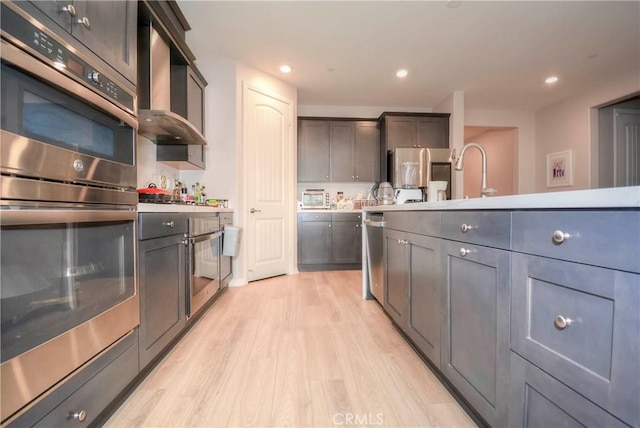 kitchen featuring wall chimney exhaust hood, sink, stainless steel appliances, and light hardwood / wood-style flooring