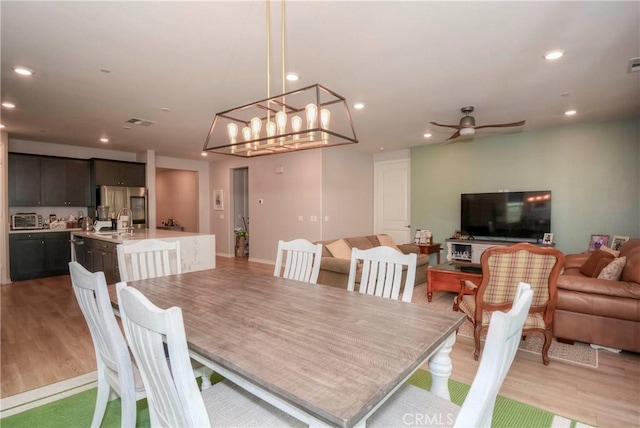 dining space featuring ceiling fan with notable chandelier and light hardwood / wood-style flooring