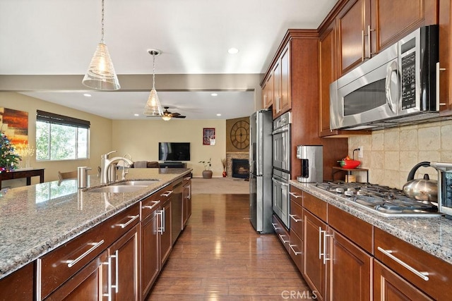 kitchen with appliances with stainless steel finishes, dark hardwood / wood-style flooring, light stone counters, sink, and hanging light fixtures