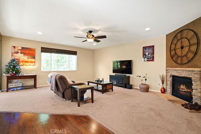 living room featuring wood-type flooring, a stone fireplace, and ceiling fan