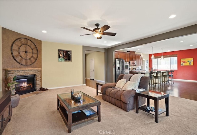 living room featuring ceiling fan, a stone fireplace, and light hardwood / wood-style flooring