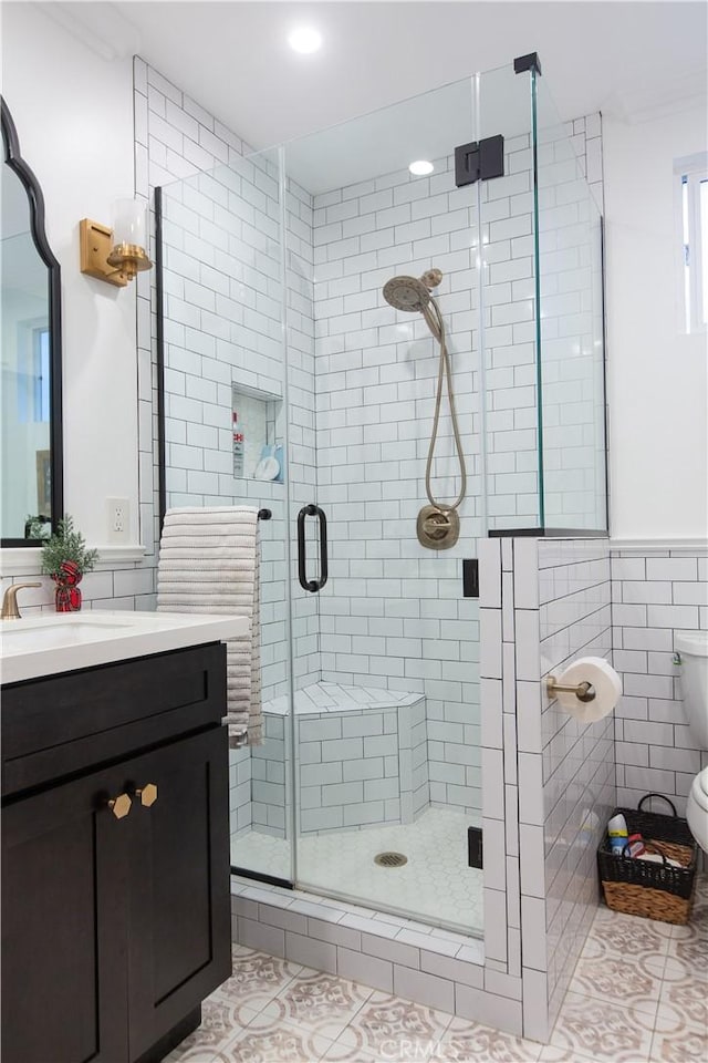 bathroom with tile patterned floors, toilet, a shower with door, vanity, and tile walls