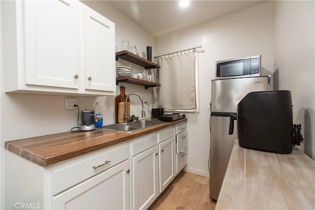 kitchen featuring wood counters, sink, light wood-type flooring, white cabinetry, and stainless steel appliances