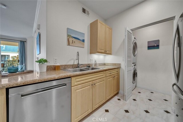 kitchen featuring sink, stacked washing maching and dryer, light stone counters, light brown cabinetry, and appliances with stainless steel finishes