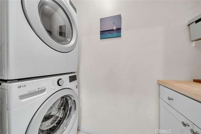 clothes washing area featuring cabinets and stacked washer / dryer