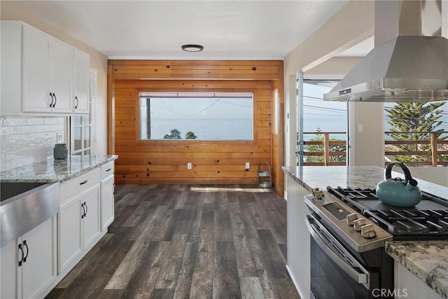 kitchen featuring island exhaust hood, white cabinetry, gas range, and wood walls