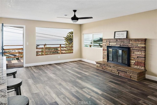 living room with dark wood-type flooring, a stone fireplace, and ceiling fan