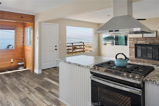 kitchen featuring wood walls, island exhaust hood, stainless steel gas stove, white cabinets, and light stone counters