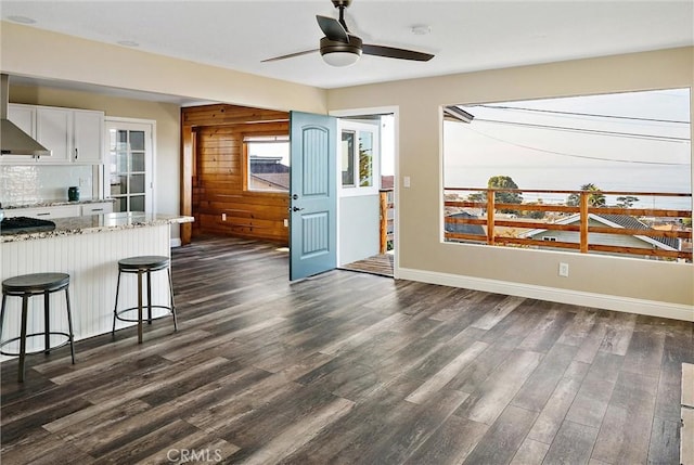 kitchen with dark hardwood / wood-style floors, a breakfast bar, wooden walls, white cabinets, and light stone counters