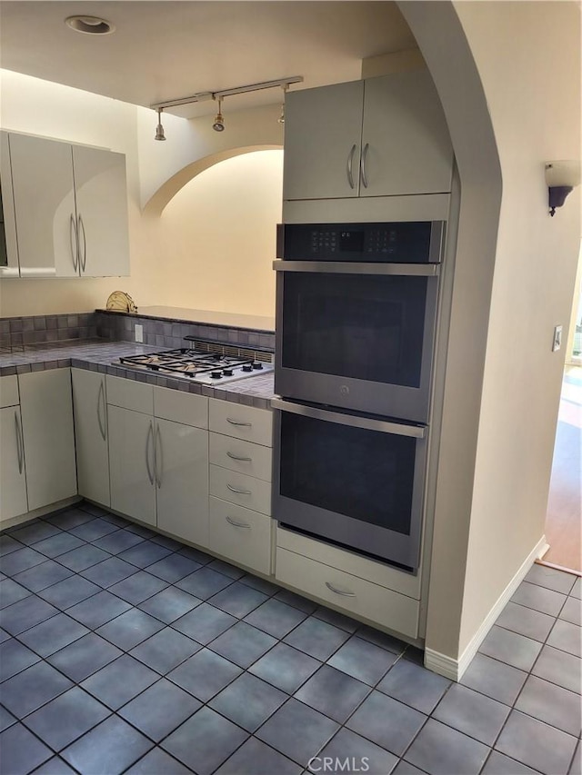 kitchen featuring stainless steel appliances, white cabinets, light tile patterned flooring, and tile countertops