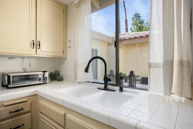 details with tile countertops, sink, and cream cabinetry