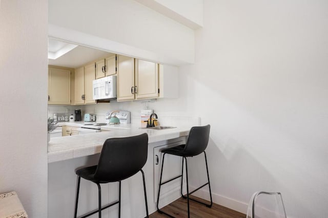 kitchen featuring sink, dark wood-type flooring, a kitchen breakfast bar, cream cabinets, and white appliances