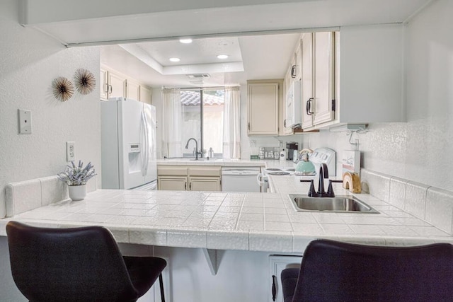 kitchen featuring tile counters, a kitchen bar, white appliances, and kitchen peninsula