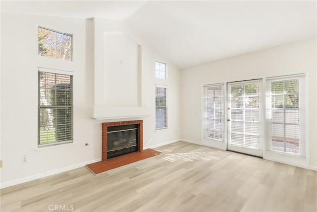 unfurnished living room featuring a fireplace, plenty of natural light, high vaulted ceiling, and light hardwood / wood-style floors