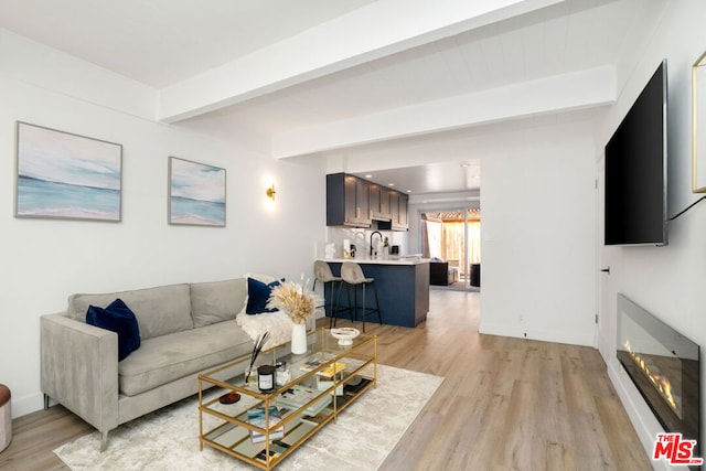 living room with light hardwood / wood-style floors, beamed ceiling, and sink