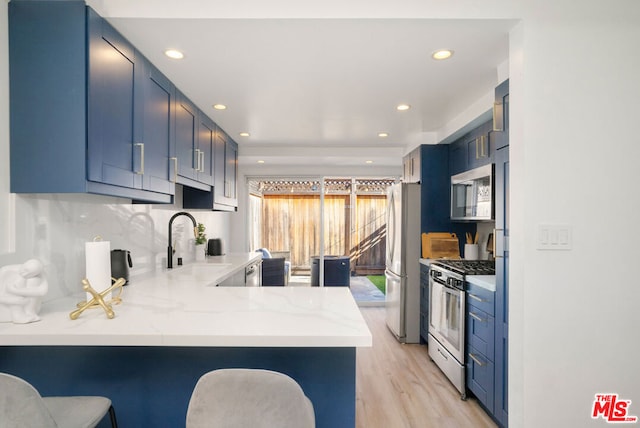 kitchen with kitchen peninsula, appliances with stainless steel finishes, sink, blue cabinetry, and a breakfast bar area