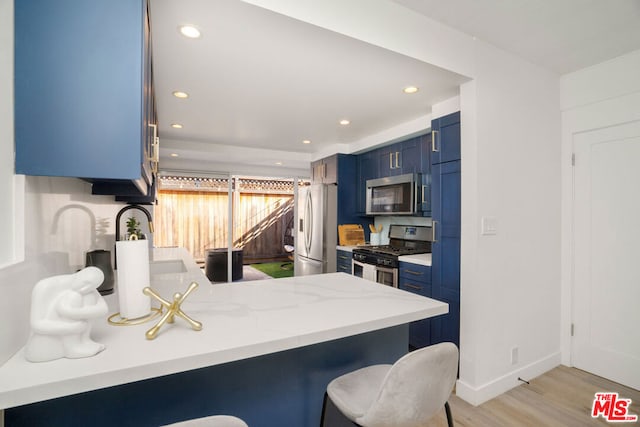 kitchen with appliances with stainless steel finishes, a kitchen bar, blue cabinetry, kitchen peninsula, and light hardwood / wood-style flooring