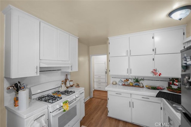 kitchen featuring white gas range, stainless steel refrigerator, light hardwood / wood-style flooring, backsplash, and white cabinets