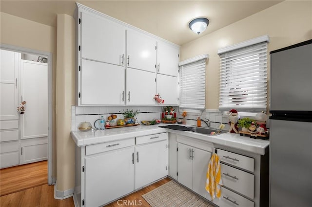 kitchen featuring white cabinets, stainless steel fridge, light wood-type flooring, and backsplash