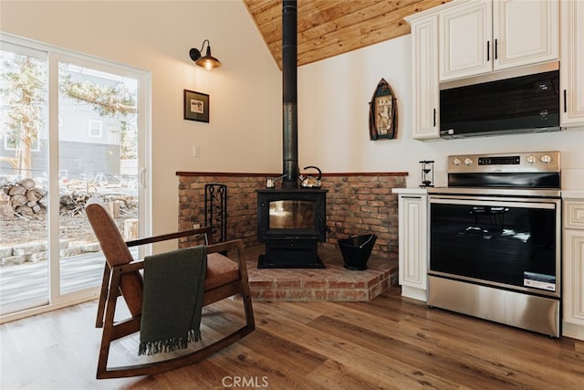 interior space with a wood stove, lofted ceiling with beams, hardwood / wood-style floors, wood ceiling, and appliances with stainless steel finishes