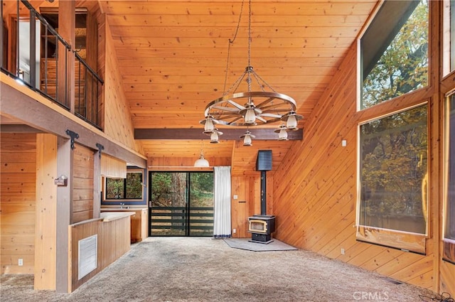 unfurnished living room with wooden walls, carpet floors, high vaulted ceiling, and a wood stove